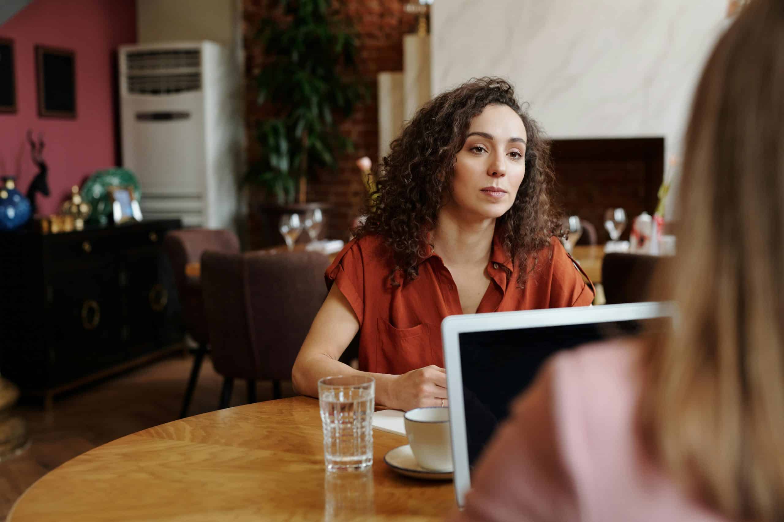 vrouw aan tafel in gesprek met iemand die niet in beeld is.